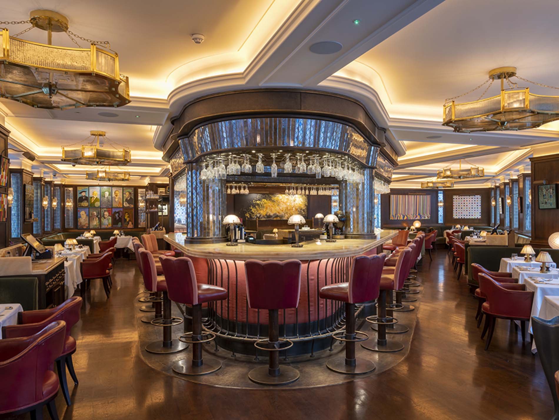 The central bar and red leather stools under brass chandeliers at The Ivy