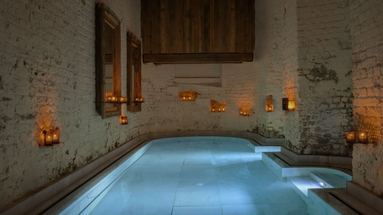 A candlelit thermal pool between whitewashed brick walls at AIRE Ancient Baths London